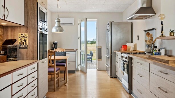 Une cuisine moderne avec des meubles en bois, des appareils électroménagers en acier inoxydable et un coin repas offrant une vue sur l’extérieur.