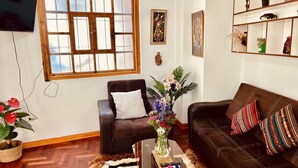 A living room with a brown leather sofa, a brown leather armchair, a coffee table with a vase of flowers, and a television mounted on the wall. - Relax in San Blas - 3-Bedroom Apartment with Views 🌅 (Cusco)