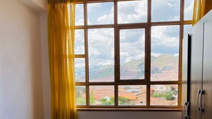 A bedroom with a bed, a window with curtains, and a view of a mountainous landscape. - Relax in San Blas - 3-Bedroom Apartment with Views 🌅 (Cusco)