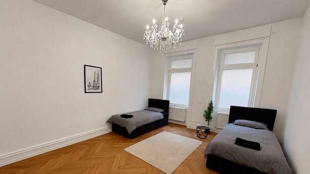Une chambre avec deux lits, un lustre, un tableau encadré et de grandes fenêtres.