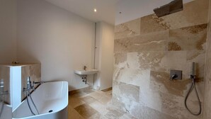 Une salle de bain moderne avec une baignoire sur pieds, un lavabo sur colonne et un espace douche agrémenté d’un mur en pierre.
