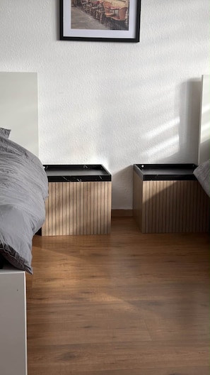 A bedroom with a bed, two bedside tables with storage, a framed picture on the wall, and a wooden floor. - Wohnung Niedernhausen 6 Betten Stellplatz (Niedernhausen)