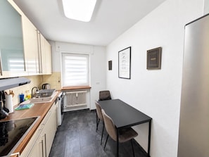 A compact kitchen with a dining area, a radiator, and a window with blinds. - Wohnung Niedernhausen 6 Betten Stellplatz (Niedernhausen)