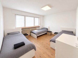 Une chambre compacte avec deux lits simples, un petit bureau blanc et un radiateur.