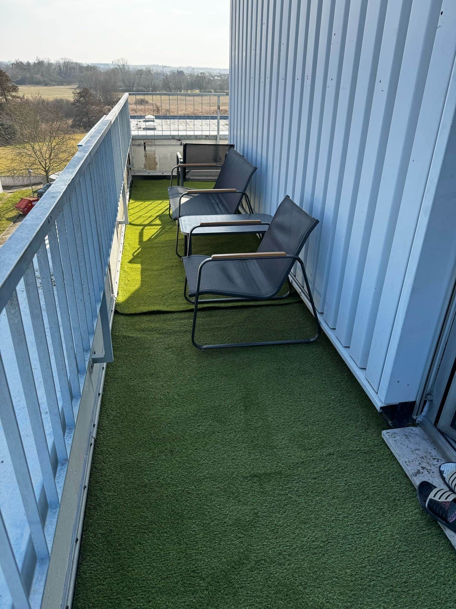 A balcony with artificial grass, metal chairs, and a metal railing.