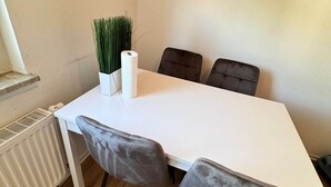 A dining area with a white table, four grey chairs, a white vase with green plants, and a white paper towel roll. - Mainz 3 Betten mit Parkplatz (Mainz)