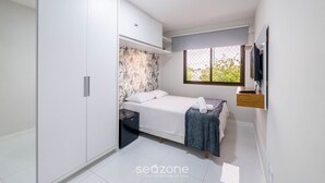 A bedroom with a bed, a wardrobe, a small desk, a window, and a TV. - Complete Apt Near Stella Maris Beach Jsm0103 (Salvador)