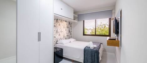 A bedroom with a bed, a wardrobe, a small desk, a window, and a TV.