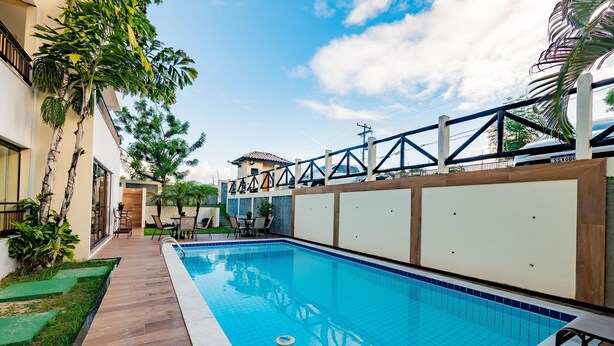 A swimming pool with a wooden deck, a covered patio area, and a view of a residential building. - Complete Apt Near Stella Maris Beach Jsm0103 (Salvador)