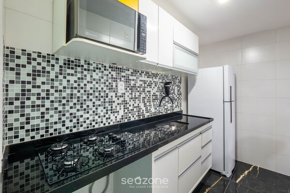Eine moderne Küche mit schwarzem Arbeitsplatz, einem Gasherd, einer Mikrowelle und einem Kühlschrank.