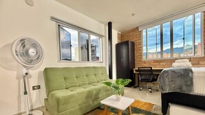 A modern living room with a green sofa, a white table, a fan, and a view of a cityscape through large windows. - Edificio RG33 (Medellín)