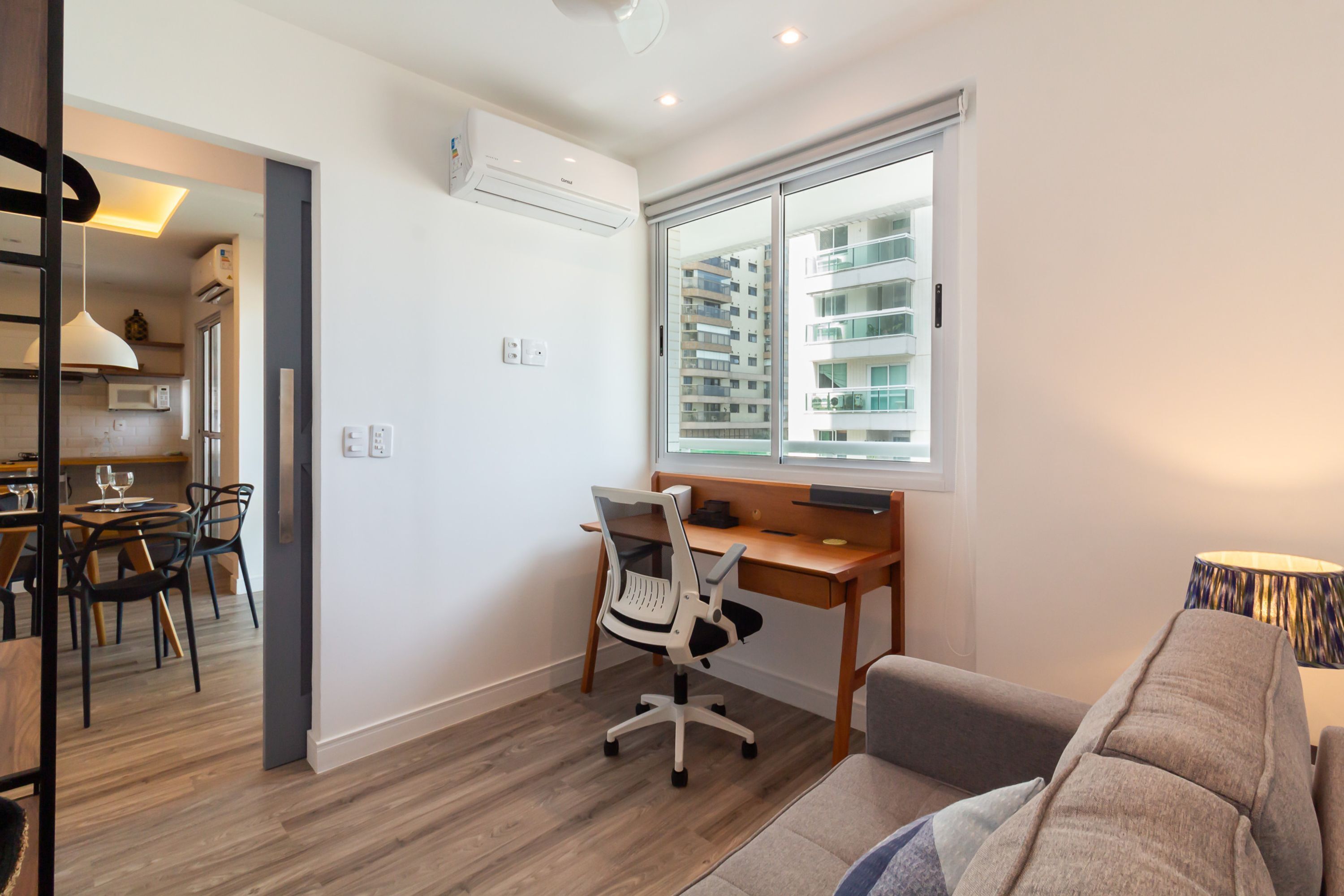 A modern living room with a wooden desk, a comfortable sofa, and a dining area with a table and chairs.