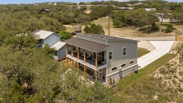 Une maison à deux étages avec un balcon, entourée d’arbres et sous un ciel dégagé.