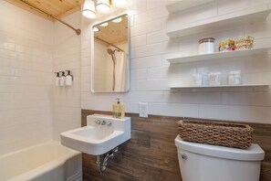 Ein modernes Badezimmer mit einem weißen Waschbecken, einer Holz-Kommode und einem Spiegel. An der Wand befinden sich Toilettenartikel und Regale über der Toilette.