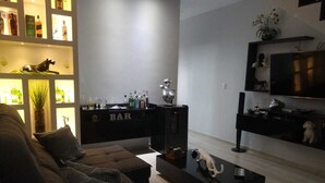 A modern living room with a sofa, a coffee table, a TV, and a bar area with bottles.