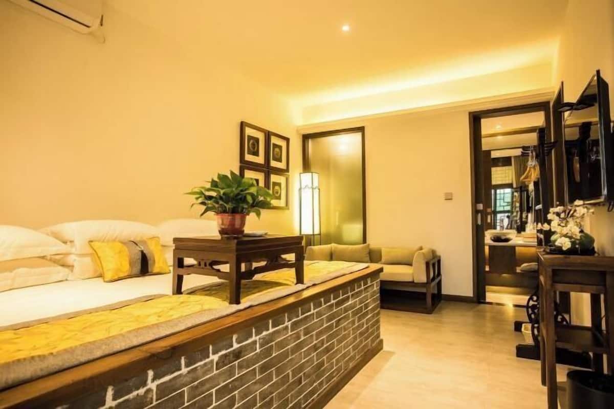 A hotel room with a bed, a small table with a plant, a sofa, a mirror, and a wall-mounted TV.