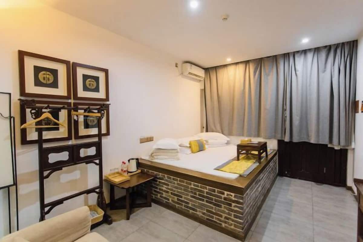 A hotel room with a bed, a small table, a chair, a coat rack, and a wall-mounted air conditioner.