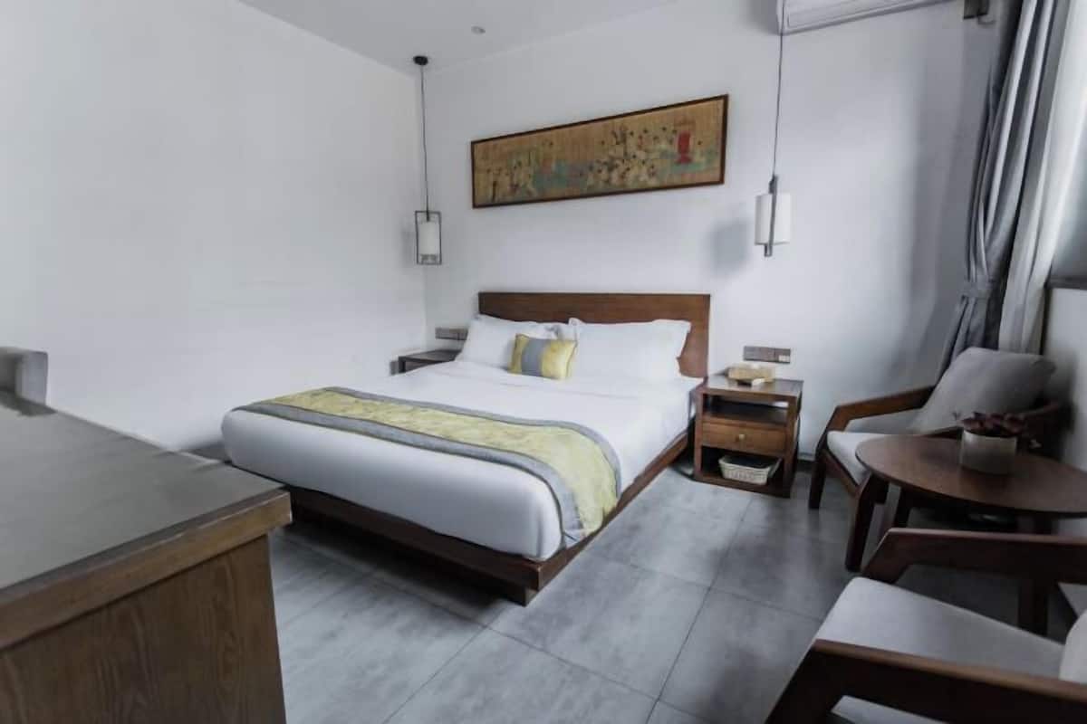 A hotel room with a bed, bedside tables, a desk, a chair, and a painting on the wall.