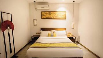 Habitación de hotel con una cama grande, una mesita de noche, un ventilador de aire acondicionado y una obra de arte colgada en la pared.