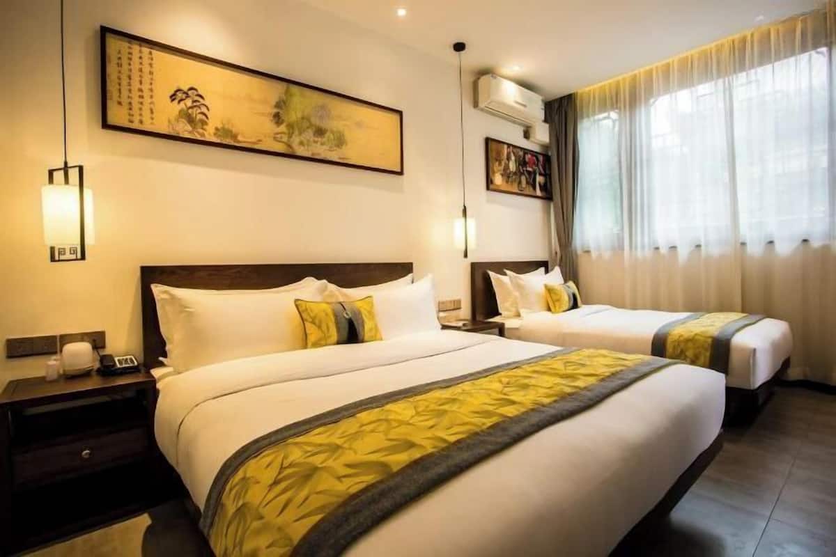 A hotel room with two beds, a large painting, an air conditioning unit, and a window with curtains.