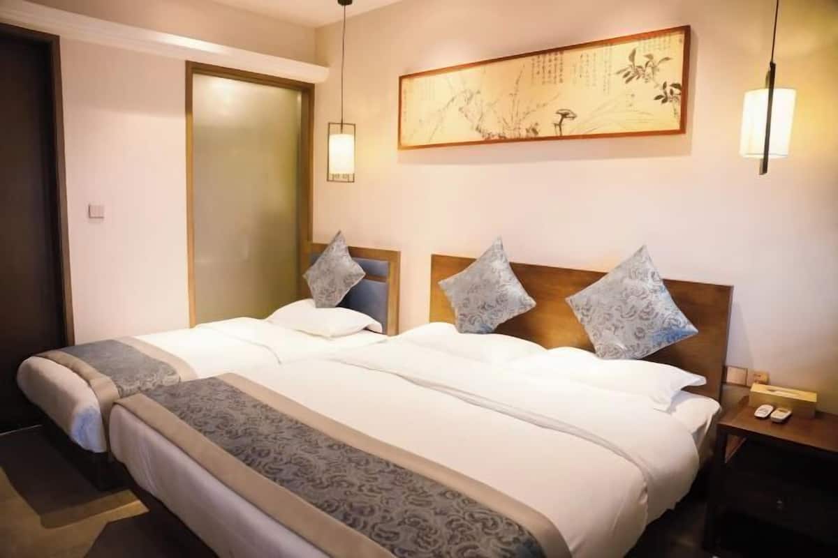 A hotel room with two beds, a wooden headboard, a wall-mounted artwork, and a bedside table with a lamp.