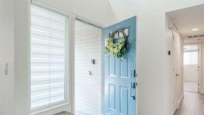 Un pasillo con una puerta azul, paredes blancas y un banco.