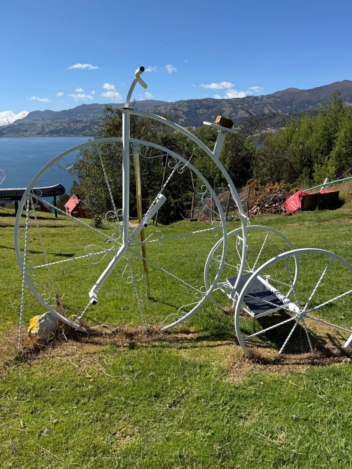 A metal sculpture of a bicycle in a grassy field with a lake and mountains in the background.