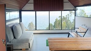 A modern interior with a high ceiling, a sofa, a wooden table, and a large window offering a view of the sea. - SAN ALEJO ECOHOTEL (Tota)