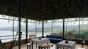 A covered outdoor seating area with tables and benches, overlooking a body of water and hills. - SAN ALEJO ECOHOTEL (Tota)