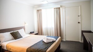A hotel room with a neatly made bed, a bedside table, a nightstand, a window with curtains, and a door. - Lilac City Motor Inn 2 Bedroom Interconnect 9/10 (Goulburn)