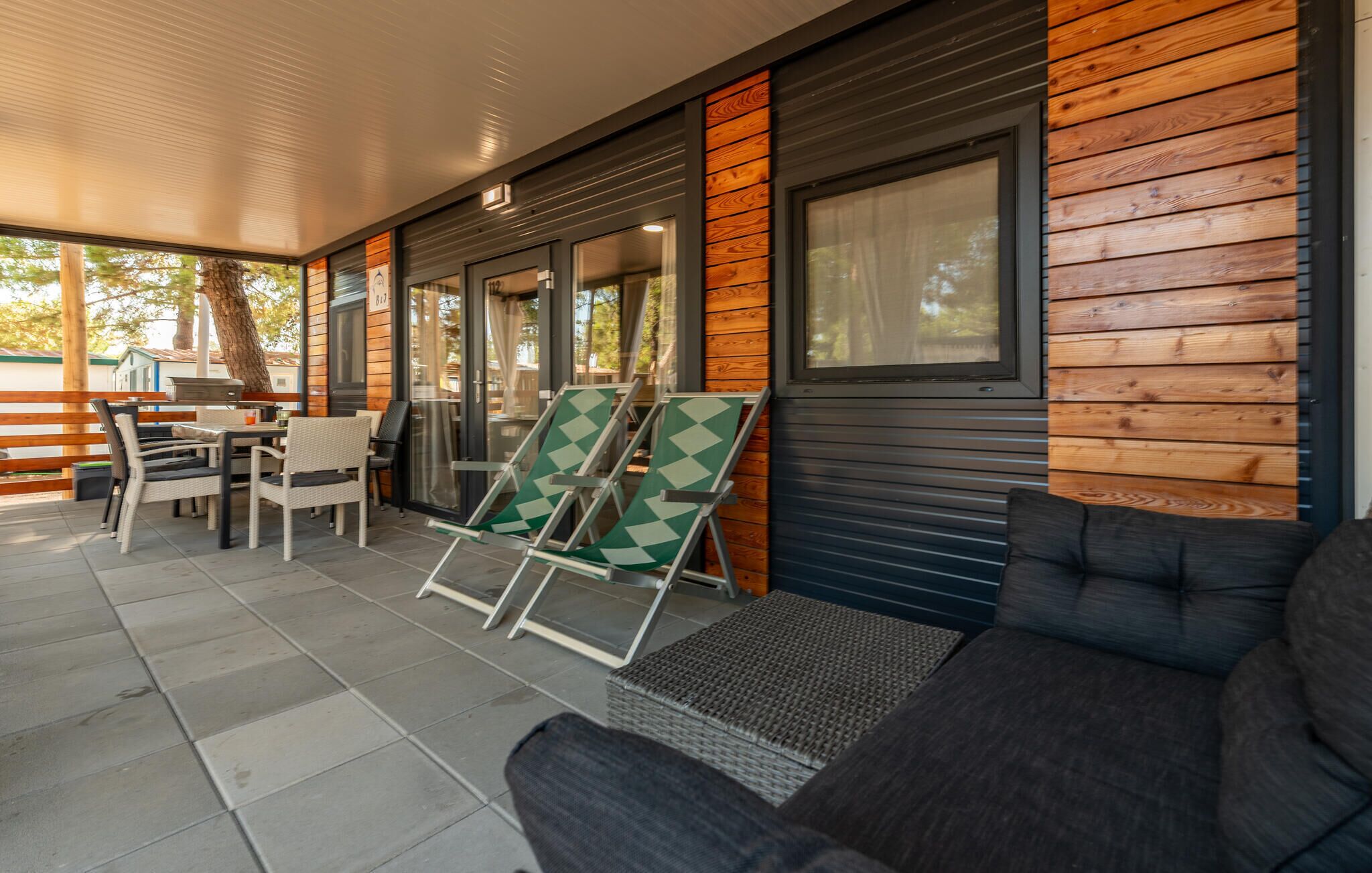 A covered outdoor seating area with wicker furniture, a grill, and a view of the surrounding area.