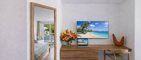 A modern bedroom with a bed, a wooden desk, a laptop, a TV, and a flower vase.