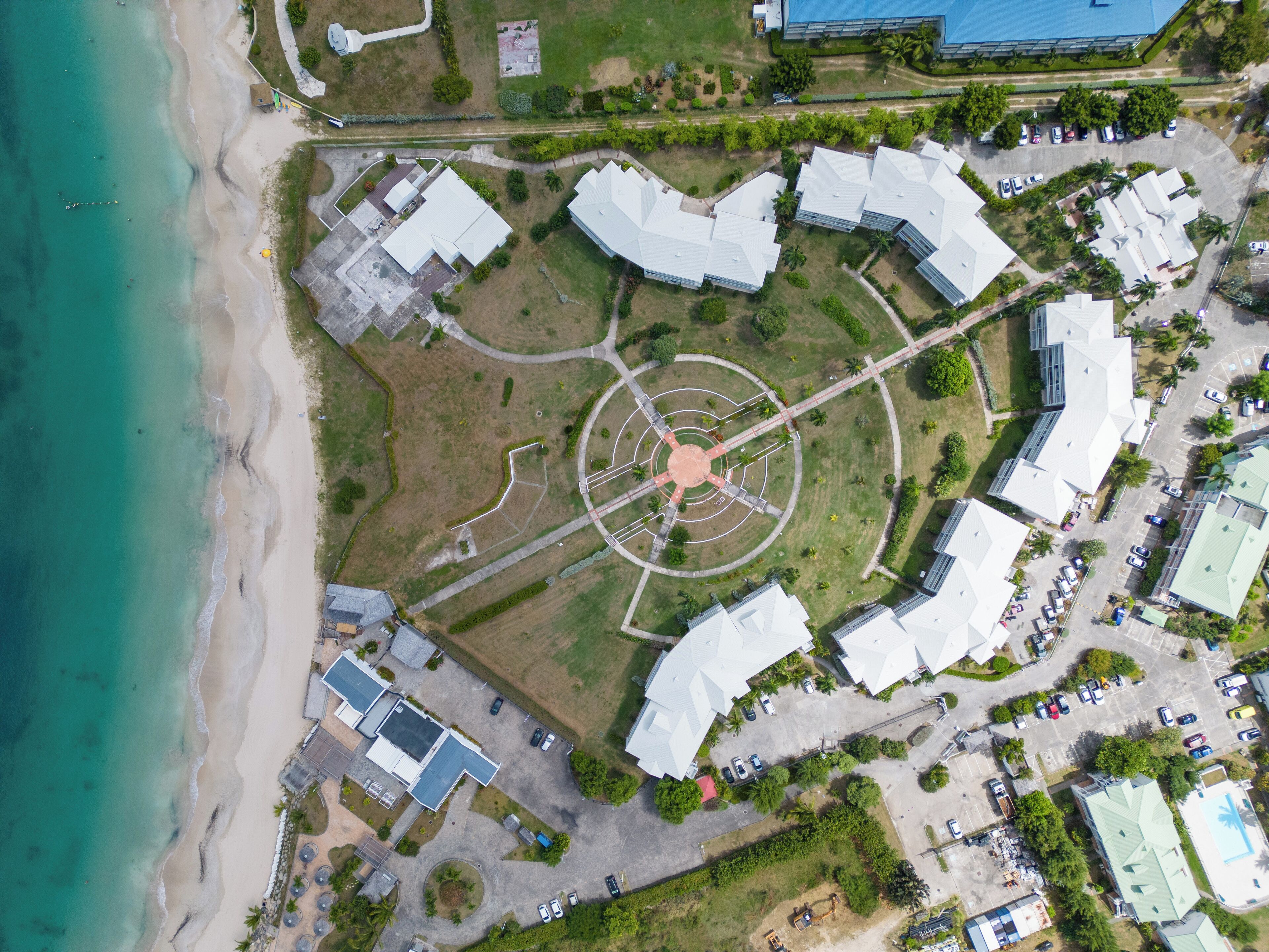 An aerial view of a coastal property with a central circular plaza, surrounding buildings, and a beach.