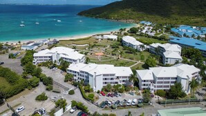 An aerial view of a coastal resort with multiple buildings, a beach, and boats in the water. - Anse Marcel Cove Suites St. Martin (Anse Marcel)