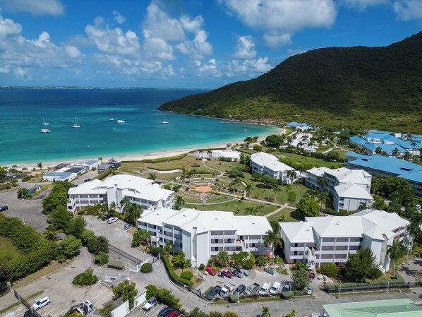 An aerial view of a coastal resort with multiple buildings, a beach, and boats in the water. - Anse Marcel Cove Suites St. Martin (Anse Marcel)