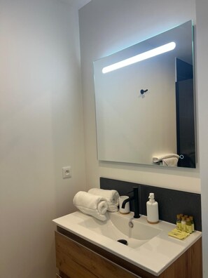 A bathroom with a white sink, a mirror, a towel rack, and a bottle of hand soap. - Anse Marcel Cove Suites St. Martin (Anse Marcel)