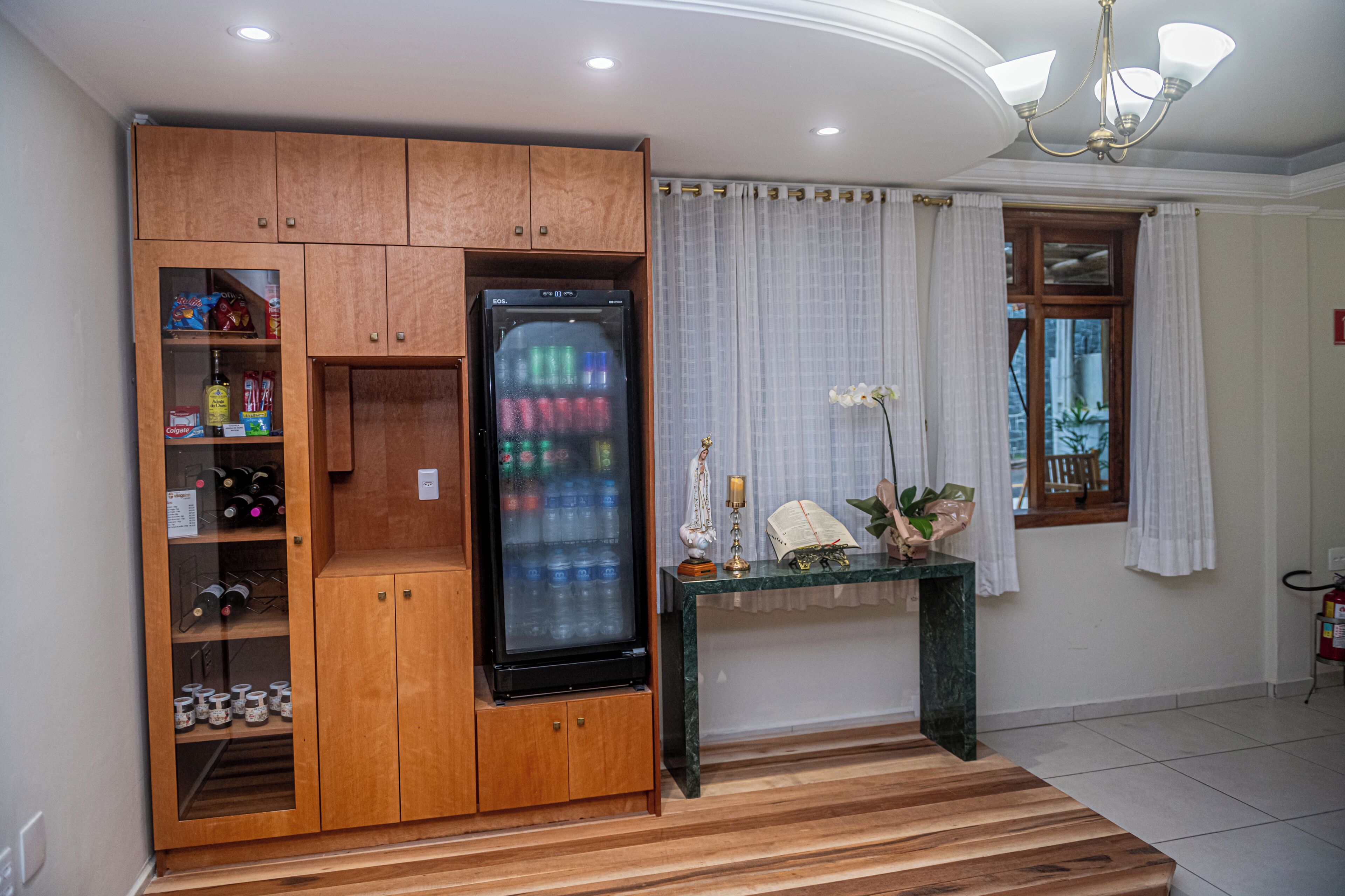 Un espace de vie compact doté d’un réfrigérateur intégré, de meubles de rangement en bois, d’une console en marbre et d’une fenêtre avec des rideaux.