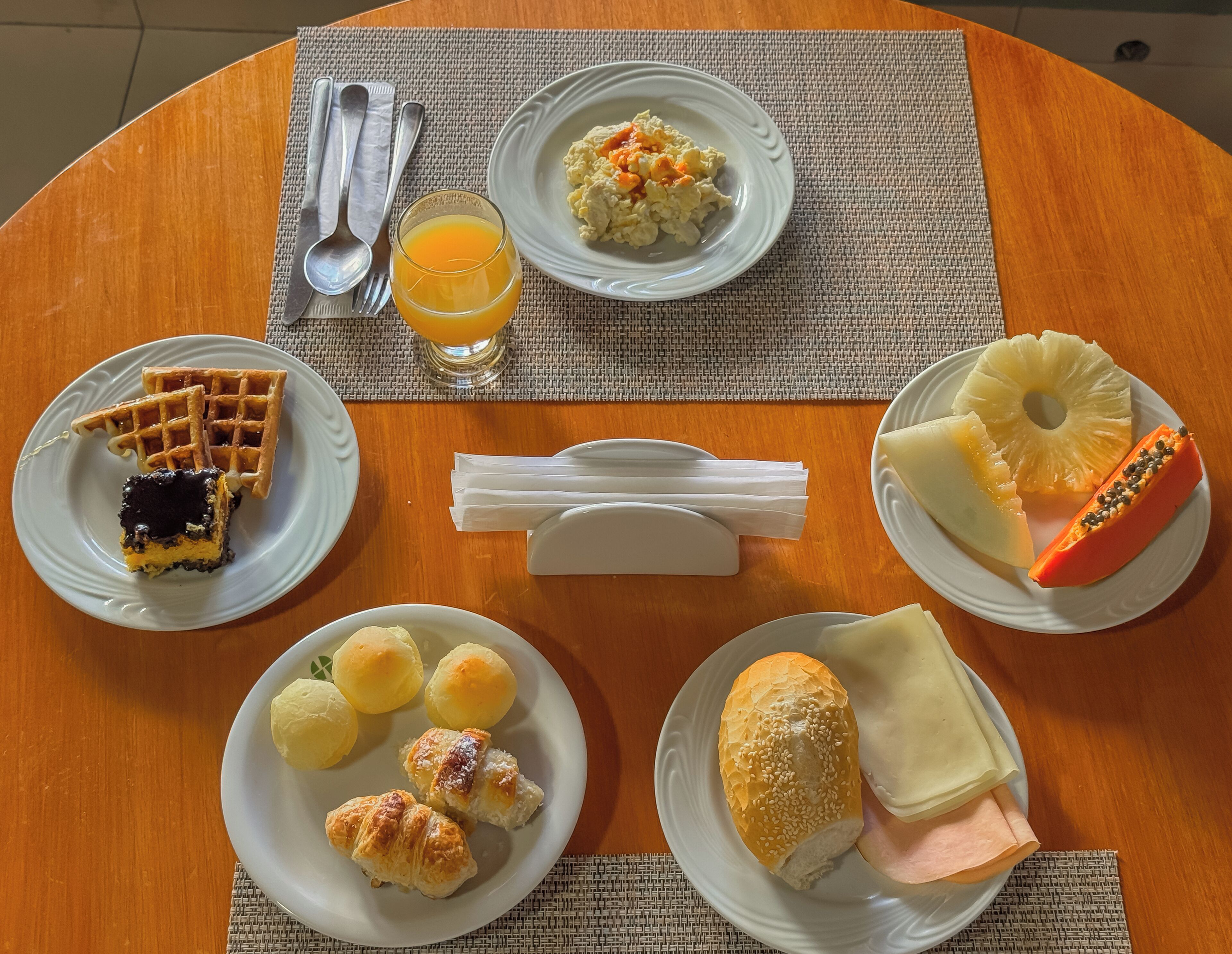 Een ontbijttafel met wafel, roerei, sinaasappelsap, croissants en ananas.