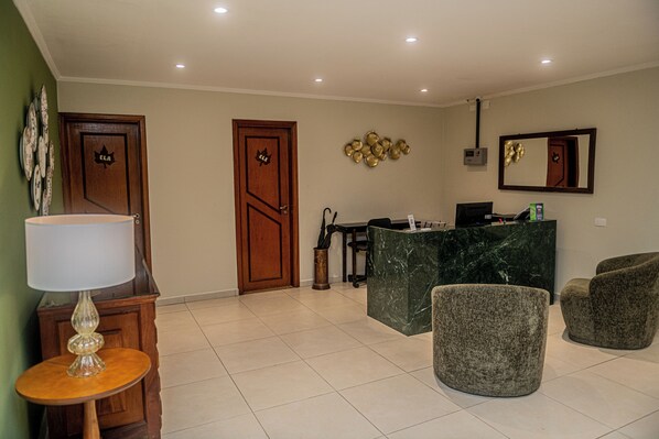 A reception area with a marble counter, two grey armchairs, a lamp, and a wall-mounted mirror. - Pousada Vilage Inn Capivari (Campos do Jordão)