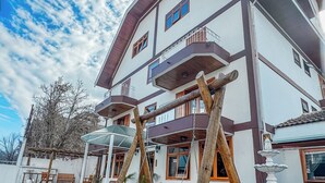 A multi-story building with balconies, a covered patio area, and a wooden swing set. - Pousada Vilage Inn Capivari (Campos do Jordão)