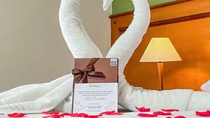 Une chambre d’hôtel avec un lit, une lampe et une carte décorative sur laquelle est disposé un ensemble de serviettes en forme de cœur.