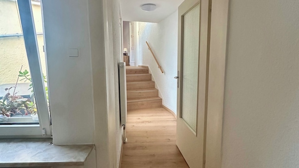 Un pasillo estrecho con escaleras de madera que llevan a una puerta con un panel de vidrio.