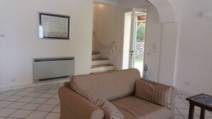 A living room with a beige sofa, a framed artwork on the wall, and a staircase leading to an outdoor area.
