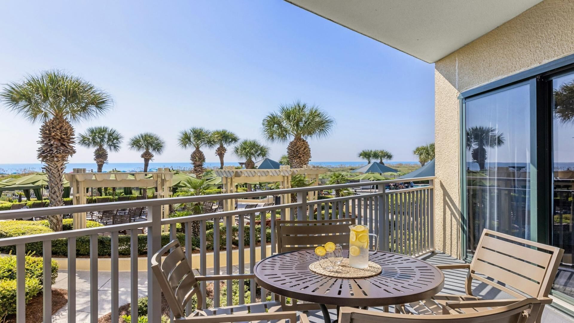 Een balkon met een tafel, stoelen en uitzicht op palmbomen en de oceaan.
