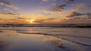 Une plage au coucher du soleil, avec des vagues et des nuages.