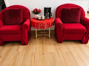 Two red armchairs with fluffy pillows, a small table with a coffee maker and a potted plant, and a red tablecloth with a rose pattern.