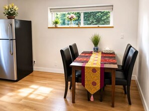 A dining area with a table set for four, a black refrigerator, and a window with plants.