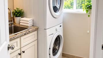 Une petite buanderie équipée d’un lave-linge, d’un évier et d’une fenêtre donnant sur un espace verdoyant.