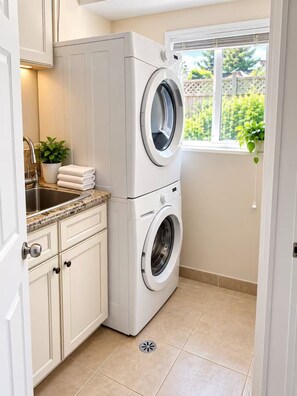 A compact laundry room with a washing machine, a sink, and a window with a view of greenery.