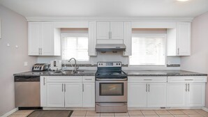 A kitchen with white cabinets, a stainless steel dishwasher, a double oven, and a granite countertop. - Cozy 2BR Villa · Garden View · Near Beach, local specialties Provided as gift 
 (Surrey)
